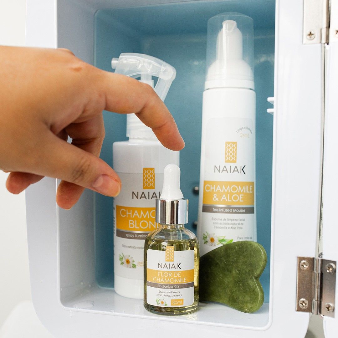 Mão pegando Chamomile Blonde, Chamomile & Aloe e Flor de Chamomile dentro de uma mini geladeira de cosméticos