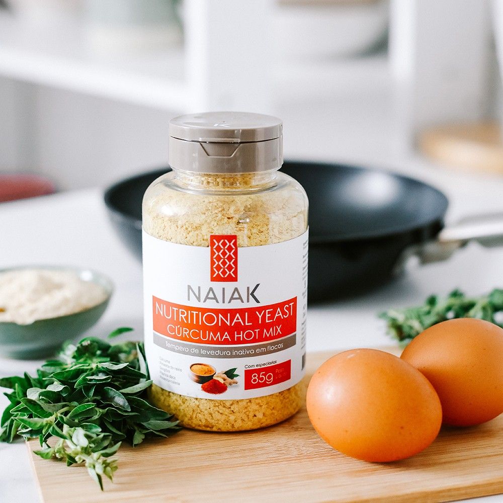 Pote de Nutritional Yeast Cúrcuma Hot Mix na bancada com ovos e ervas