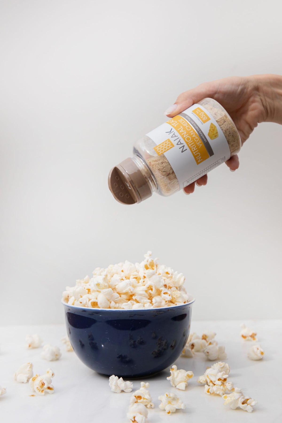 Mão polvilhando Nutritional Yeast Vegan Cheese sobre uma tigela de pipoca