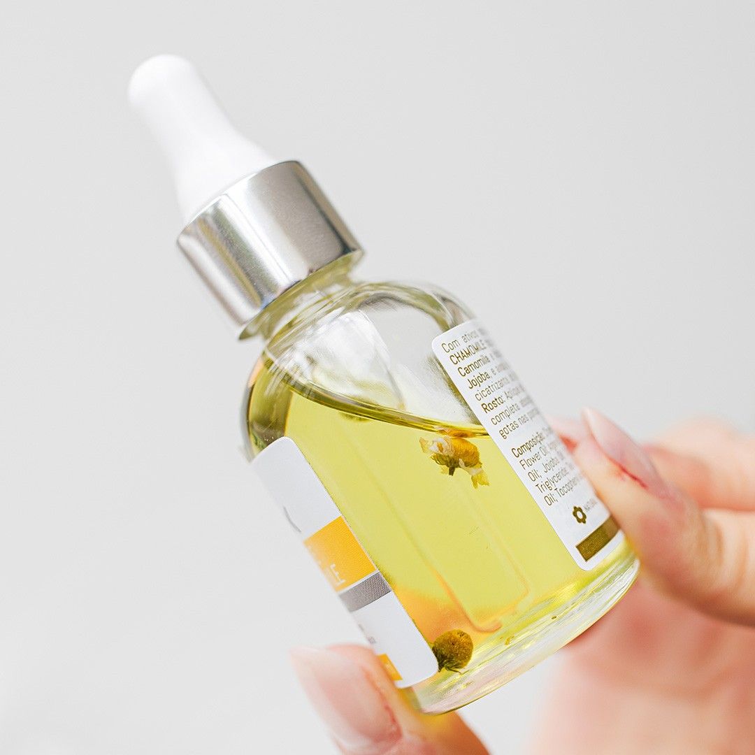 Flor de Chamomile Naiak: mão segurando o frasco conta-gotas com flores de camomila no óleo